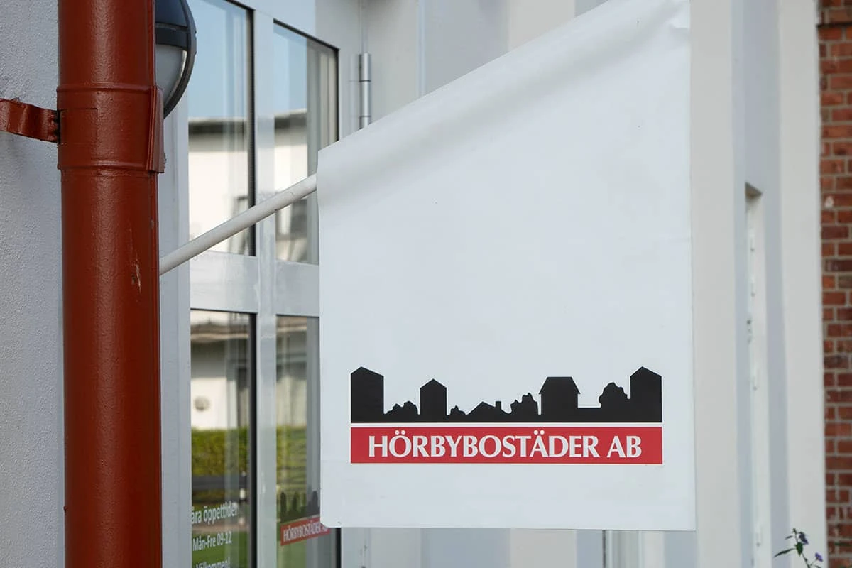 Liten vit flagga med Hörbybostäders logotyp hänger från en fasad.