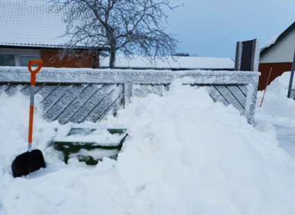 Stor snöhög vid ett plank. Ett snöskyffel står nertryckt i snön.